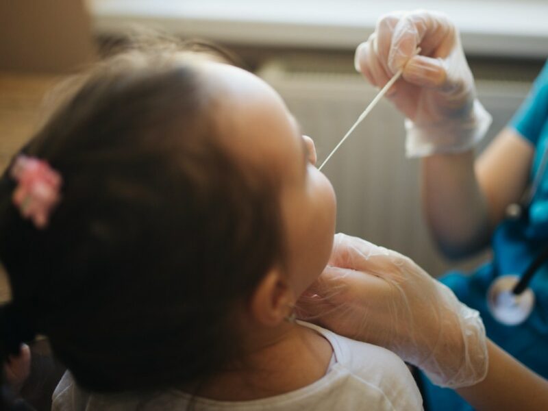 Doctor holds swab for mucus sample from kid nose or mouth closeup back view. Nenad Stojkovic, flickr https://creativecommons.org/licenses/by/2.0/