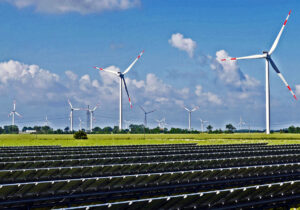 Solar panels, wind turbines, and an electricity pylon; unidentified location. Commons, by hpgruesen.